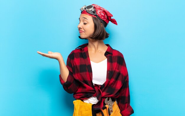 Young latin woman feeling happy and smiling casually, looking to an object or concept held on the hand on the side