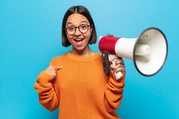 Young latin woman feeling happy, surprised and proud, pointing to self with an excited, amazed look