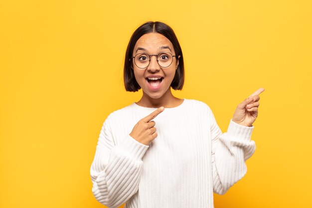 Young latin woman feeling joyful and surprised, smiling with a shocked expression and pointing to the side