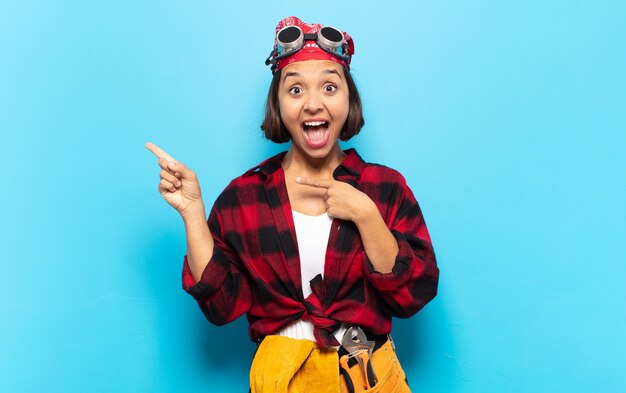 Young latin woman feeling joyful and surprised, smiling with a shocked expression and pointing to the side