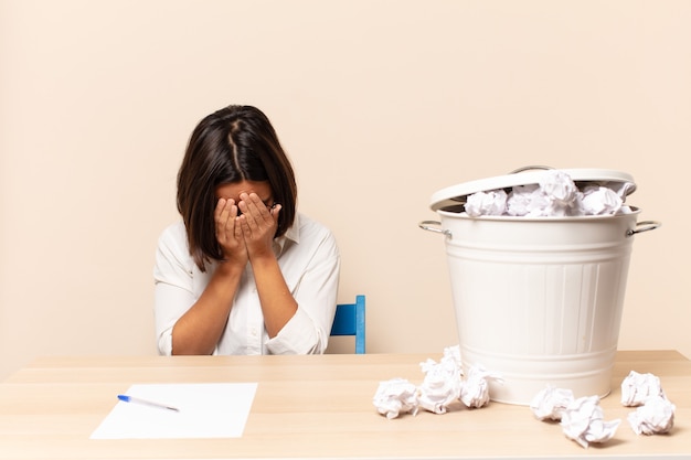 Young latin woman feeling sad, frustrated, nervous and depressed, covering face with both hands, crying