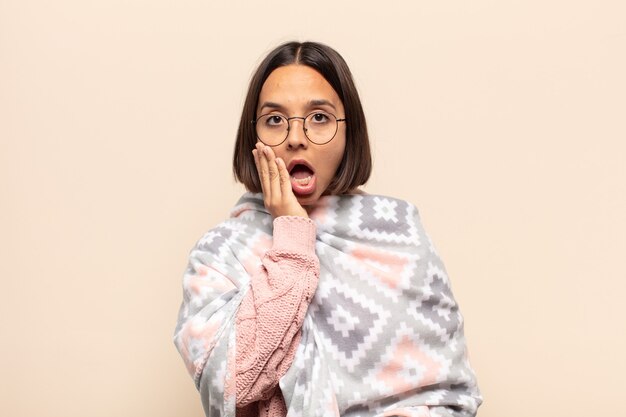 Young latin woman feeling shocked and scared, looking terrified with open mouth and hands on cheeks