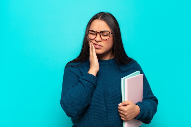 Young latin woman holding cheek and suffering painful toothache, feeling ill, miserable and unhappy, looking for a dentist