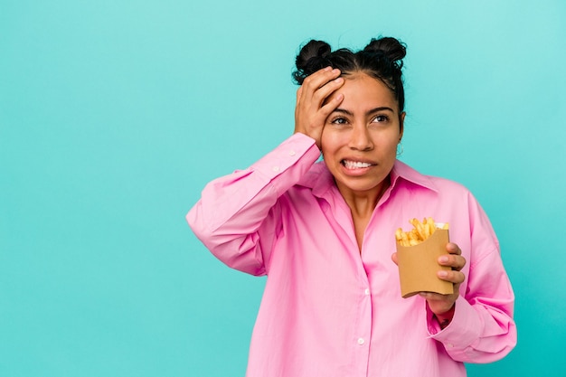 Young latin woman holding chips isolated on blue background being shocked, she has remembered important meeting.