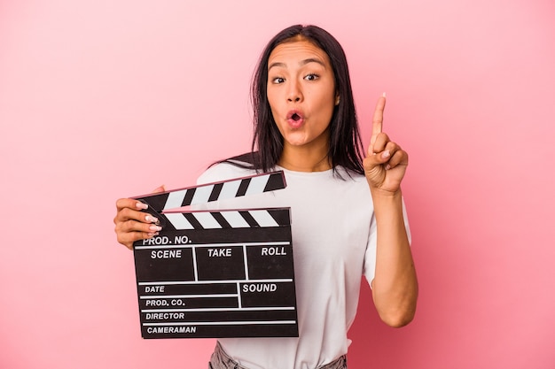 Young latin woman holding clapperboard isolated on pink background  having some great idea, concept of creativity.