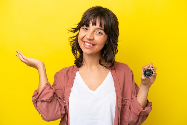 Young latin woman holding compass isolated on yellow background extending hands to the side for inviting to come