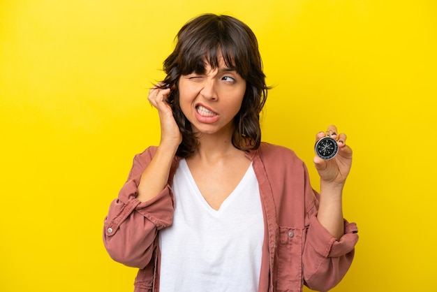 Young latin woman holding compass isolated on yellow background frustrated and covering ears