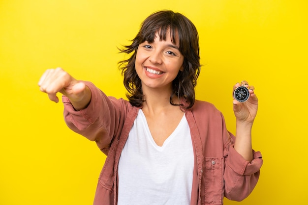 Young latin woman holding compass isolated on yellow background giving a thumbs up gesture