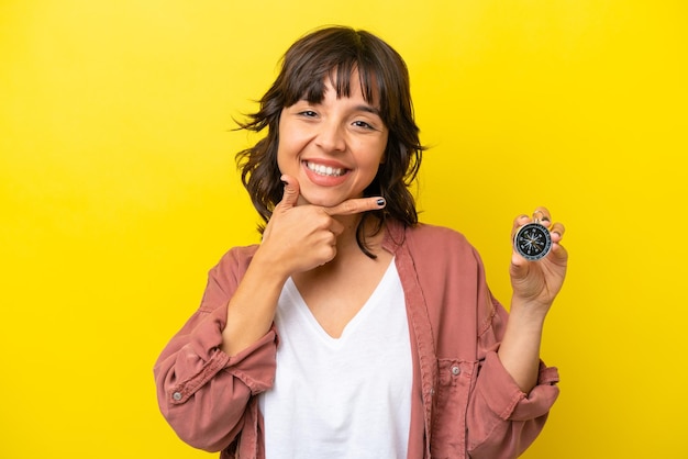 Young latin woman holding compass isolated on yellow background happy and smiling