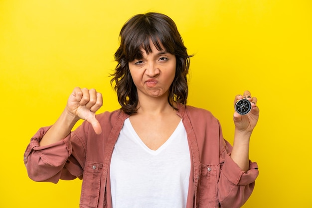 Photo young latin woman holding compass isolated on yellow background showing thumb down with negative expression