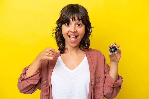 Young latin woman holding compass isolated on yellow background surprised and pointing front