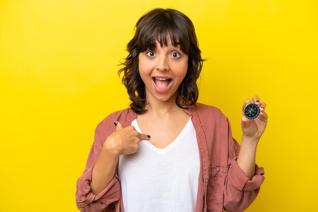 Young latin woman holding compass isolated on yellow background with surprise facial expression