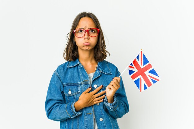 Молодая латинская женщина, держащая английский флаг, изолированный на белой стене, дует щеки, имеет усталое выражение. Концепция выражения лица.