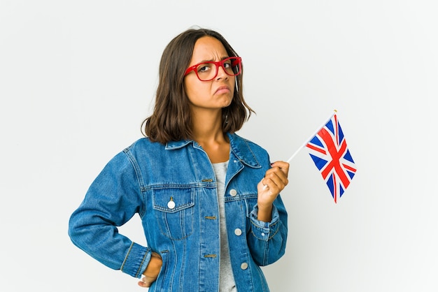 Young latin woman holding a english flag isolated on white wall frowning face in displeasure, keeps arms folded.