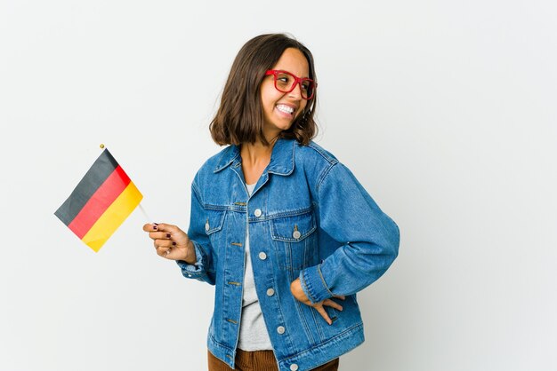 Young latin woman holding a german flag isolated on white background laughs and closes eyes, feels relaxed and happy.