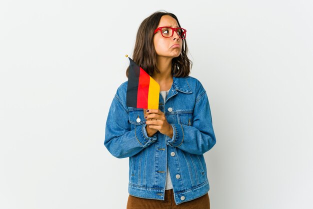 Young latin woman holding a german flag isolated on white praying, showing devotion, religious person looking for divine inspiration.