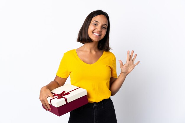 Young latin woman holding a gift isolated on white counting five with fingers