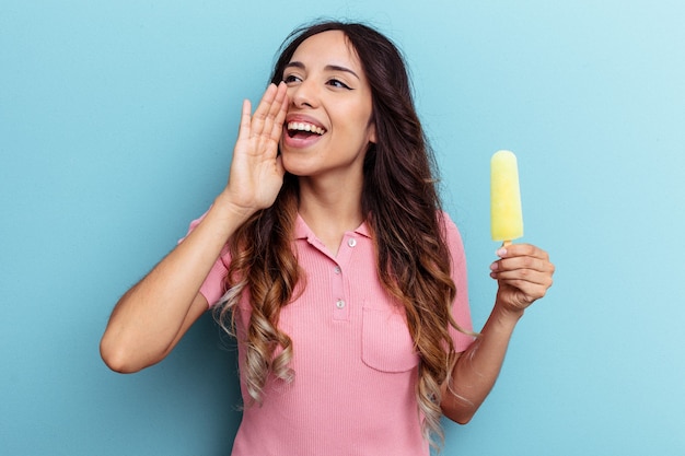 Young latin woman holding ice cream isolated on blue background shouting and holding palm near opened mouth.