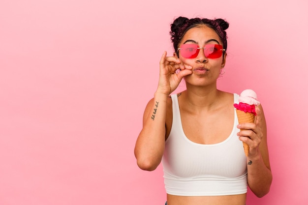 Молодая латинская женщина, держащая мороженое на розовом фоне с пальцами на губах, хранит в секрете.
