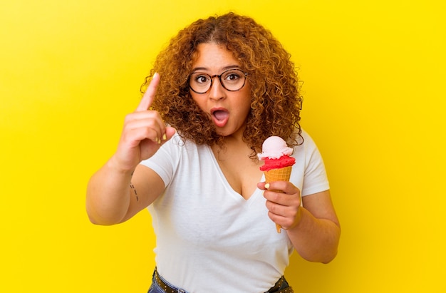 Young latin woman holding an ice cream isolated on yellow background having an idea, inspiration concept.