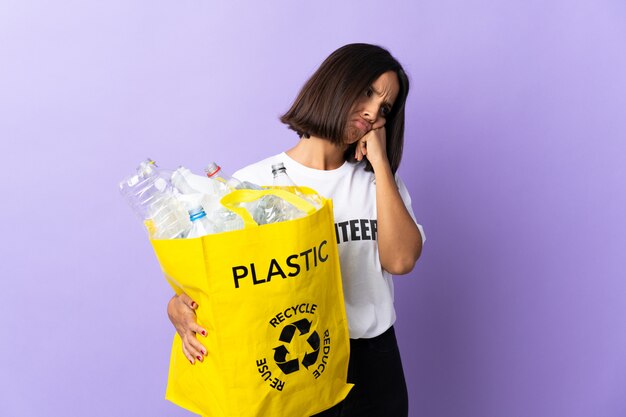 Young latin woman holding a recycling bag full of paper to recycle isolated on purple with tired and bored expression