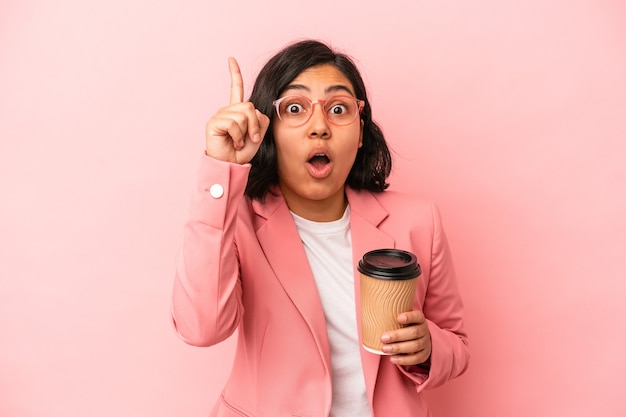 Young latin woman holding take away coffee isolated on pink background having an idea, inspiration concept.