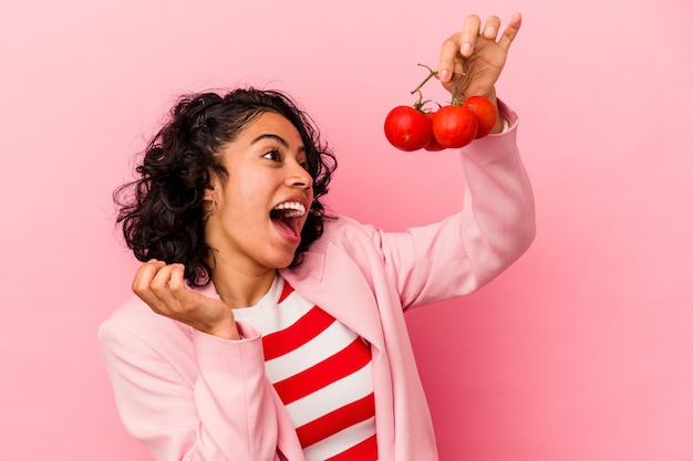 Young latin woman holding tomatoes isolated on pink background