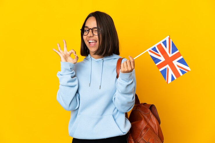 Photo 指でokサインを示す黄色の背景に分離されたイギリスの旗を保持している若いラテン女性
