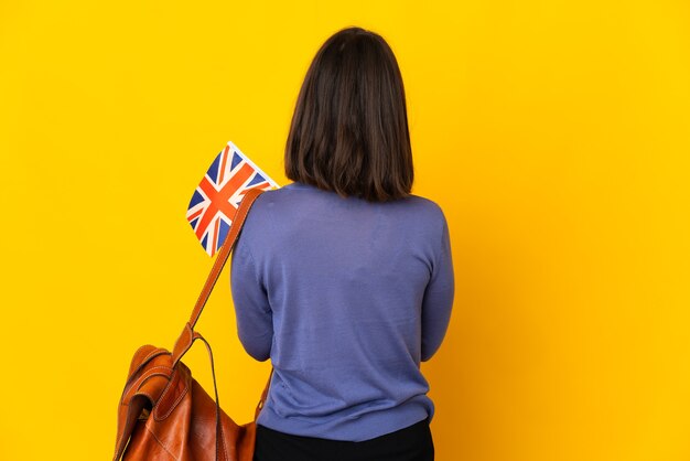 後ろの位置で黄色の壁に分離されたイギリスの旗を保持している若いラテン女性