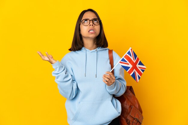 Young latin woman holding an United Kingdom flag isolated on yellow wall stressed overwhelmed