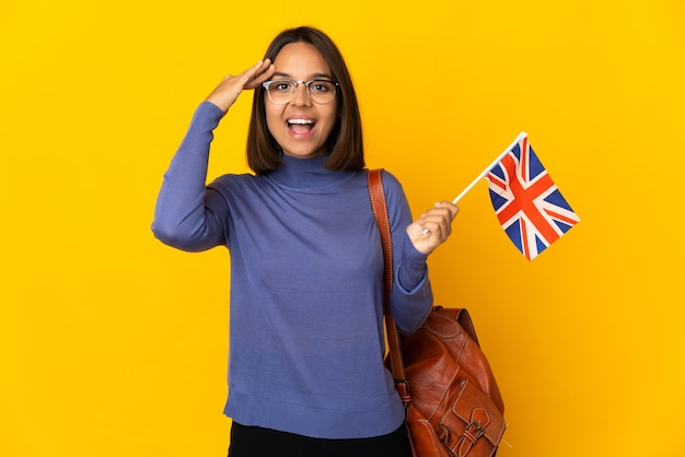 Young latin woman holding an United Kingdom flag isolated on yellow wall with surprise expression