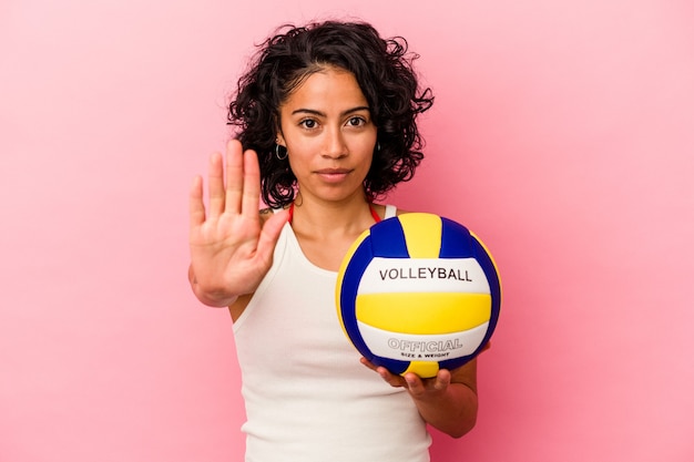 Young latin woman holding a volley ball isolated on pink\
background standing with outstretched hand