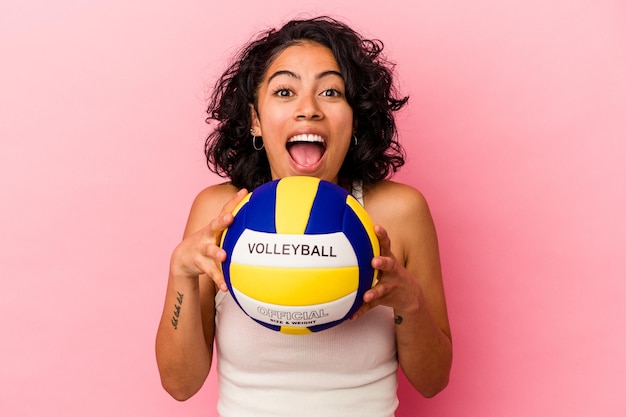 Young latin woman holding a volley ball isolated on pink background