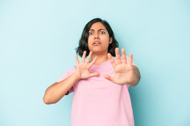 Young latin woman isolated on blue background being shocked due to an imminent danger