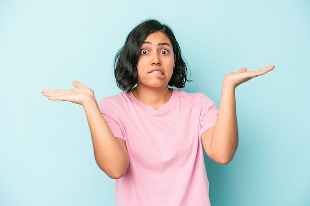 Young latin woman isolated on blue background confused and doubtful shrugging shoulders to hold a copy space.