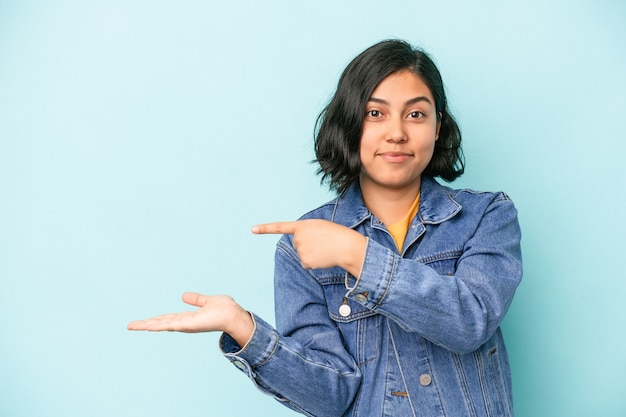 Young latin woman isolated on blue background excited holding a copy space on palm.