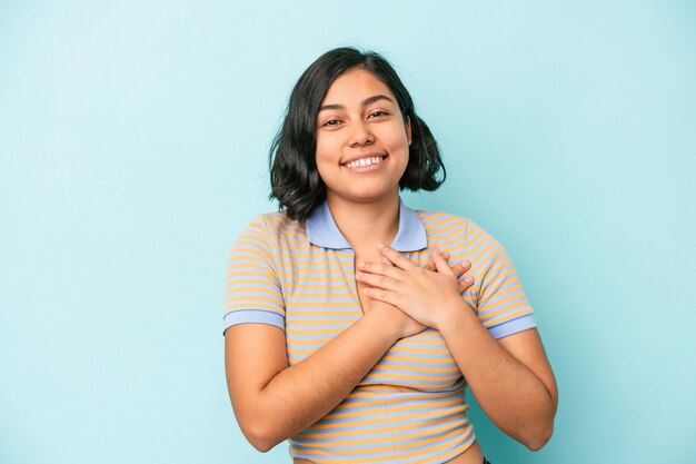 Young latin woman isolated on blue background has friendly expression, pressing palm to chest. Love concept.