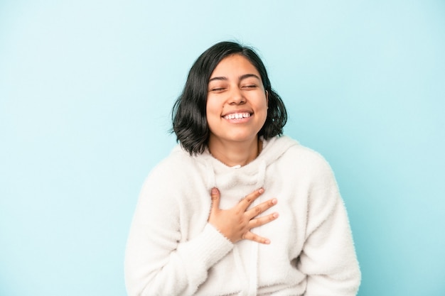 Young latin woman isolated on blue background laughs out loudly keeping hand on chest.