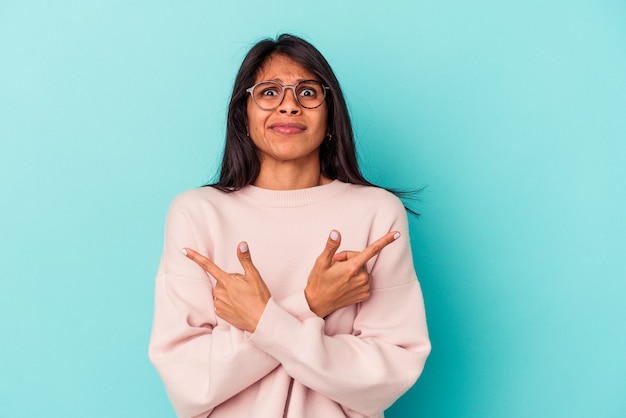 Young latin woman isolated on blue background points sideways, is trying to choose between two options.