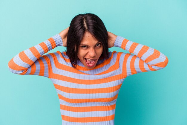 Young latin woman isolated on blue background screaming, very excited, passionate, satisfied with something.