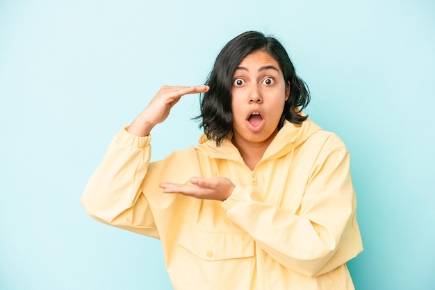 Young latin woman isolated on blue background shocked and amazed holding a copy space between hands.