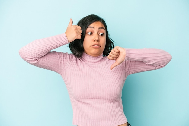 Young latin woman isolated on blue background showing thumbs up and thumbs down, difficult choose concept