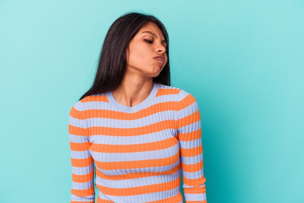 Young latin woman isolated on blue background shrugs shoulders and open eyes confused.