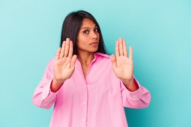 Young latin woman isolated on blue background standing with outstretched hand showing stop sign, preventing you.