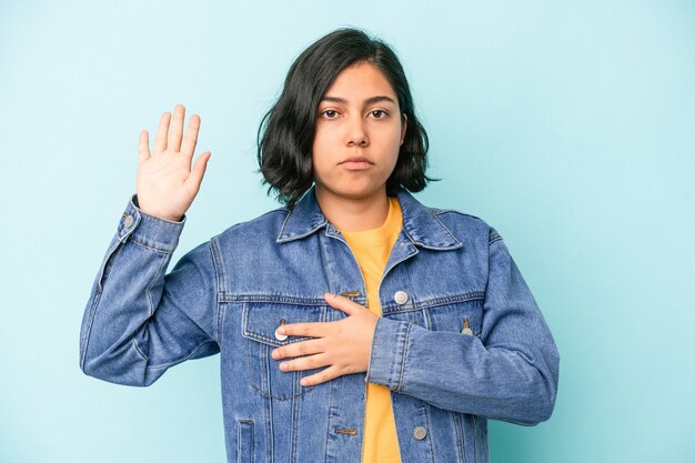 Young latin woman isolated on blue background taking an oath, putting hand on chest.