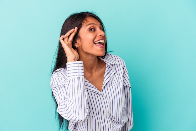 Young latin woman isolated on blue background trying to listening a gossip.