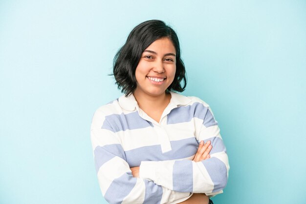 Young latin woman isolated on blue background who feels confident, crossing arms with determination.