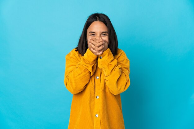 Young latin woman isolated on blue wall happy and smiling covering mouth with hands