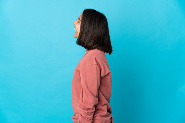 Young latin woman isolated on blue wall laughing in lateral position