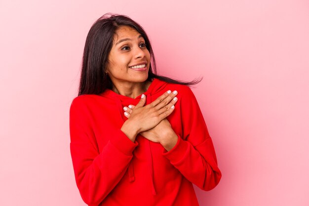 Young latin woman isolated on pink background has friendly expression, pressing palm to chest. Love concept.